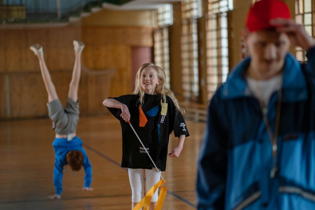 Kinder turnen in einer Sporthalle über Matten und Geräte.